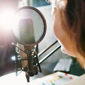 Shot of a woman speaking into a microphone in a recording studio